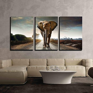 Three-panel wall art of an elephant on a road with a beige sofa and coffee table in the foreground.