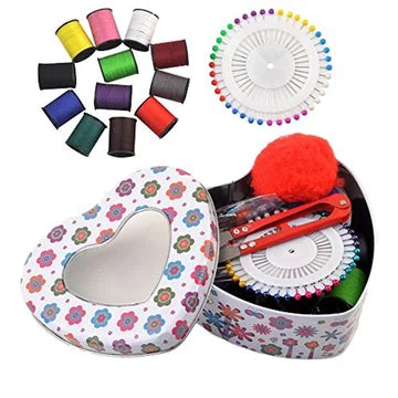 Collection of sewing accessories including colorful thread spools and a heart-shaped tin with sewing tools on a white background.