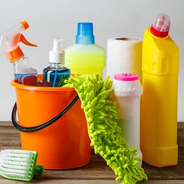 Cleaning supplies including a bucket, bottles, paper towels, and a scrub brush on a wooden surface.