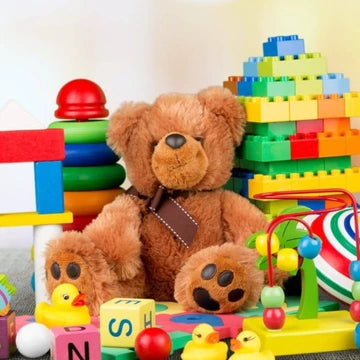 Brown teddy bear surrounded by colorful toys including blocks and rubber ducks.