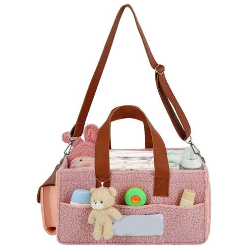 Pink baby bag with brown straps and teddy bear toys on a white background