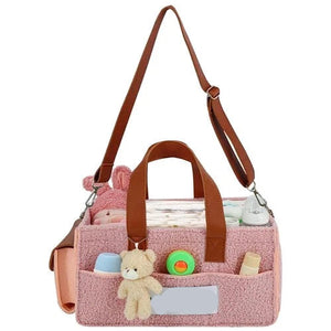 Pink baby bag with brown straps and teddy bear toys on a white background